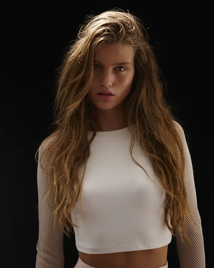 Jeune femme aux cheveux châtains, portant un haut blanc et une jupe blanche, debout dans une forêt.
